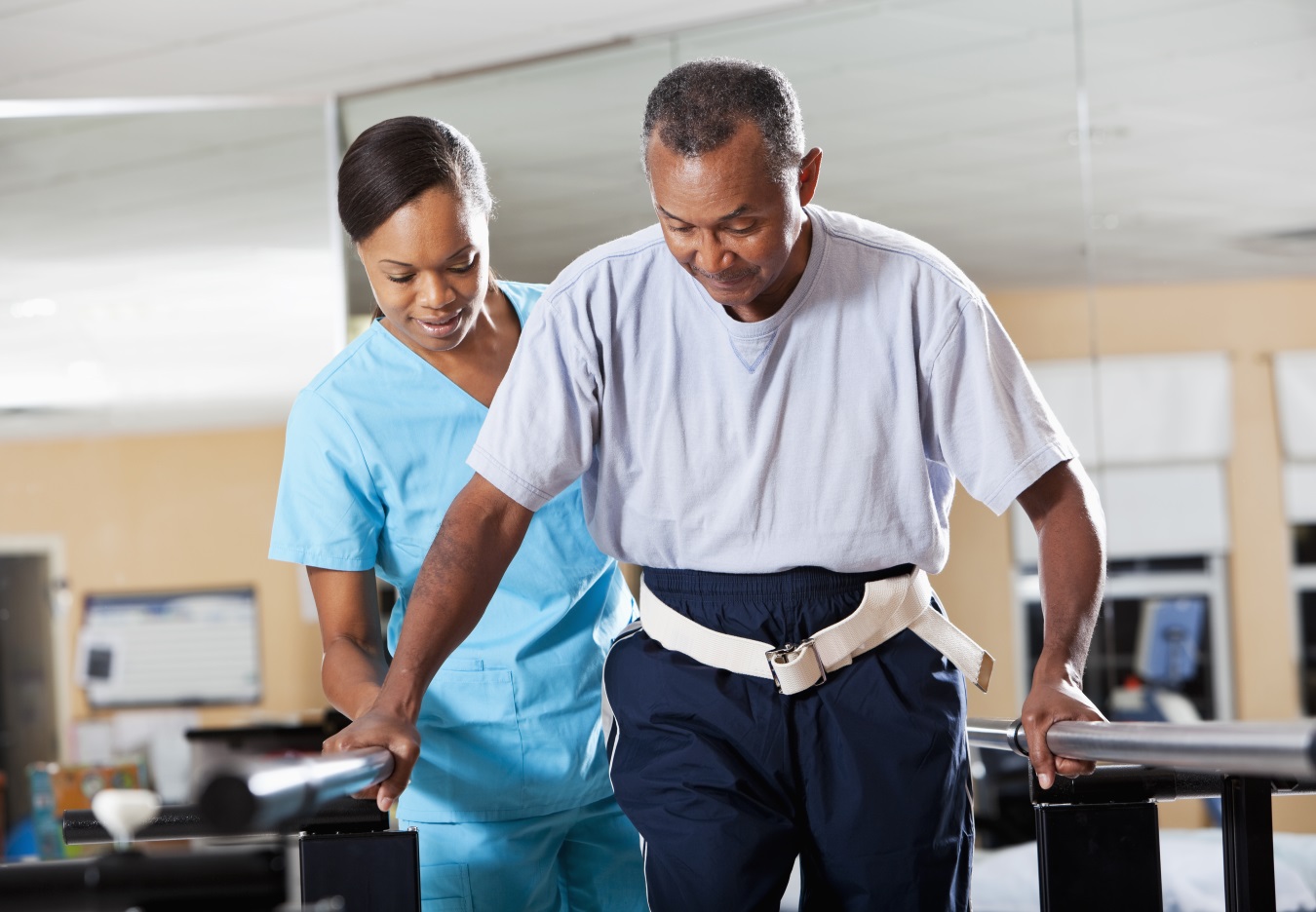 A man being assisted by a female healthcare provider as he receives rehabilitation treatment in a healthcare environment.